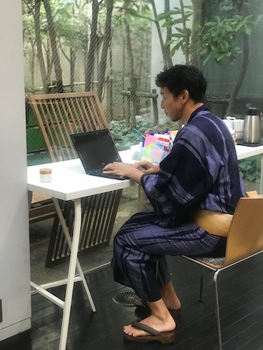 中庭に向かって浴衣姿でパソコン仕事をする山本さん